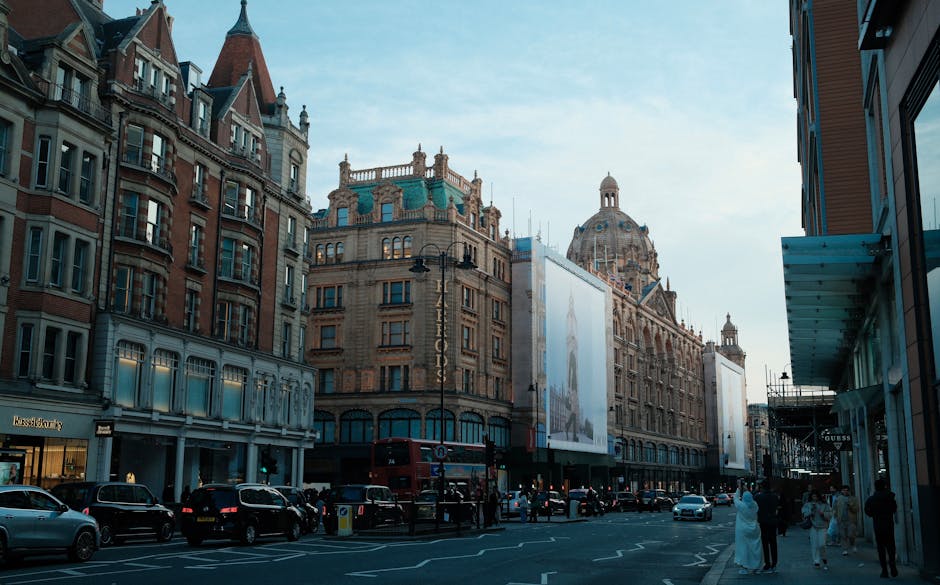 A city street scene in Knightsbridge featuring historic and modern architecture, with multi-story brick and stone buildings, some with decorative turrets and domes. The street is busy with parked cars