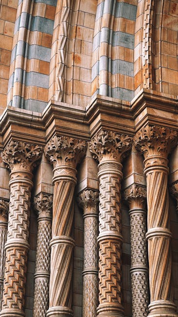 Close-up view of intricately carved stone columns displaying detailed patterns and ornate capitals, part of a historic building's exterior. The stone surfaces showcase a mix of beige and light brown t